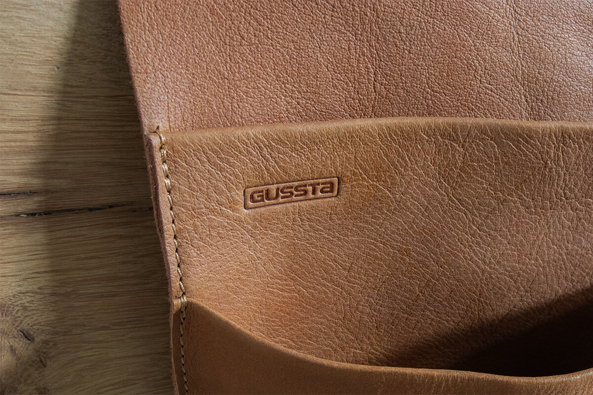 Close-up sfeerfoto van het logo op het buffelleren opbergtasje van nahka en gussta in de kleur cognac Close-up sfeerfoto van het logo op het buffelleren opbergtasje van nahka en gussta in de kleur cognac